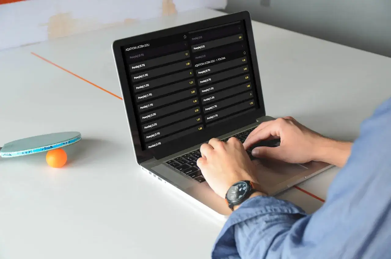 Mężczyzna analizuje kursy bukmacherskie na laptopie, widoczne są opcje