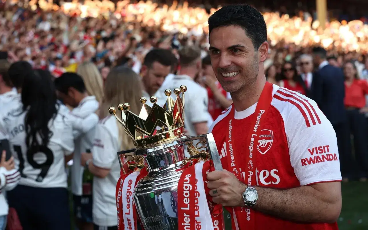 Mikel Arteta, trener Arsenalu, z dumą trzyma puchar Premier League. Tłum kibiców świętuje sukces.